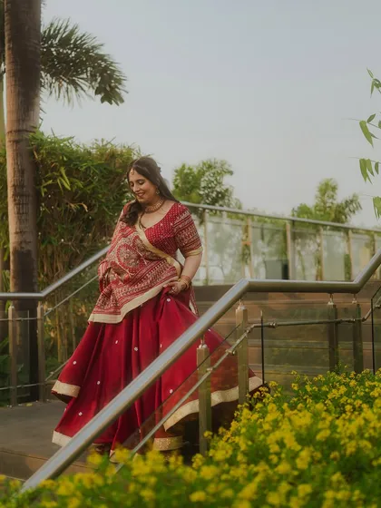 The bride walks down a staircase, her red lehenga creating a beautiful flow of movement. This candid shot captures her grace and the joyful anticipation of her wedding day.