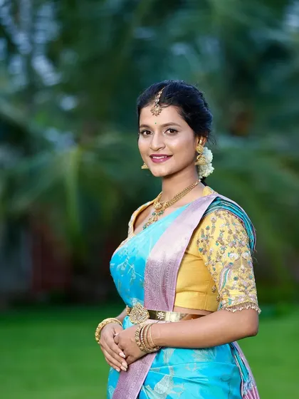 The beautiful bride-to-be Kavya glows in a sky-blue designer silk saree for her engagement. Paired with a contrasting yellow embroidered blouse, this look is both vibrant and traditionally elegant.
