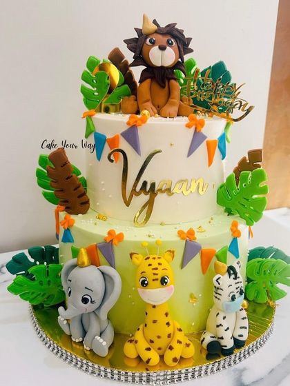 A whole jungle party on a two-tier cake. This design features adorable fondant animals like a lion, elephant, and giraffe, perfect for a wild and fun-filled birthday.