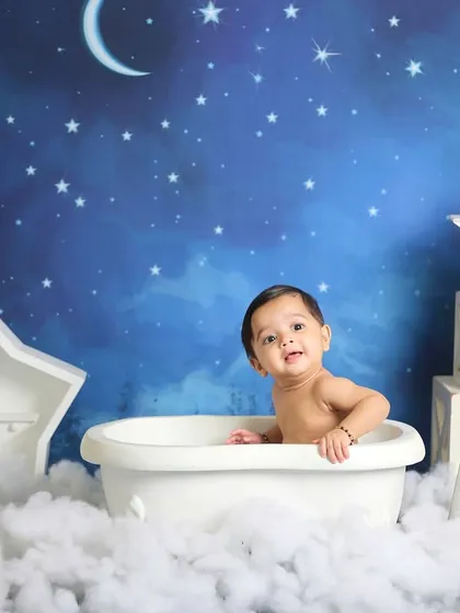 A whimsical "bath time" shot from a celestial-themed session. The baby is sitting in a mini tub amidst clouds, under a starry night sky.