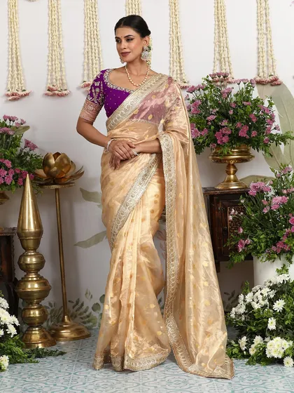 The ethereal beauty of this ivory organza saree is elevated by a contrasting deep purple embroidered blouse. It is a testament to understated luxury, perfect for intimate celebrations where grace and sophistication are key.