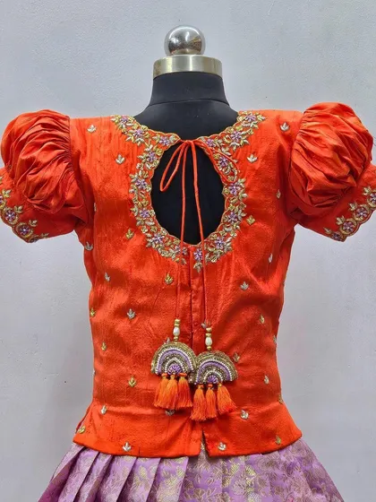 A detailed view of the back of an orange blouse, showing the keyhole design and the intricate embroidery around the neckline.