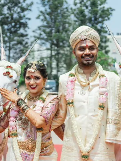 A joyful moment from a wedding procession. The groom looks radiant in his custom ivory silk sherwani and matching embroidered turban, designed for a traditional South Indian ceremony.