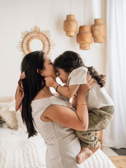 A mother and her son share a sweet forehead kiss in the cozy boho bedroom setup.