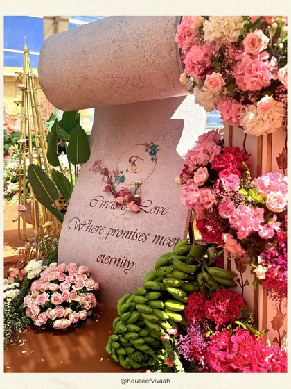 A personalized stone-carved scroll reads "Circle of Love," surrounded by pink florals and traditional elements like bananas, adding a unique and symbolic detail to the wedding ceremony.