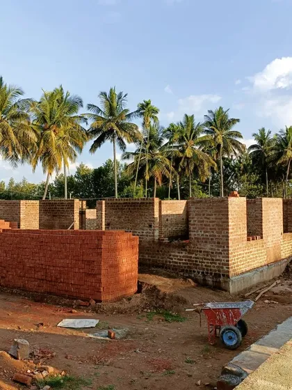 The walls of the Samyak Yoga center rising against a backdrop of palm trees. The bricks are laid with a traditional lime mortar mix, which includes jaggery and local herbs to improve its strength.