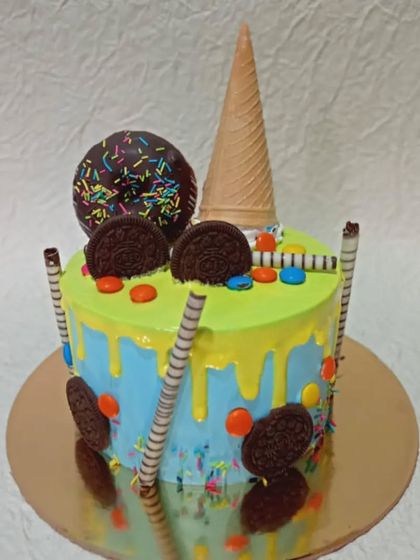 A colorful and fun drip cake loaded with treats. It's topped with a donut, an ice cream cone, Oreo cookies, and candy, making it a dream for anyone with a sweet tooth.