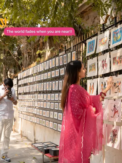 A candid moment captured at an outdoor art gallery in Mumbai. The groom-to-be is seen taking a photo of his fiancée, a sweet role-reversal that tells a story within a story.