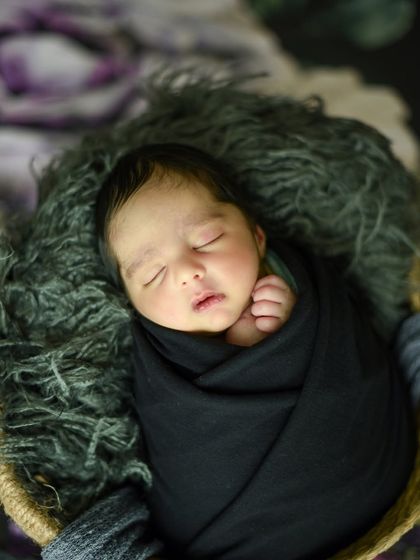A close-up portrait in the black wrap, focusing on the baby's serene sleeping face and tiny hand.