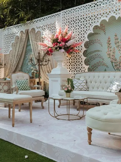 A luxurious seating area with a pastel blue peacock-themed wallpaper backdrop. The design combines classic furniture with vibrant floral arrangements and elegant candelabras for a touch of royalty.