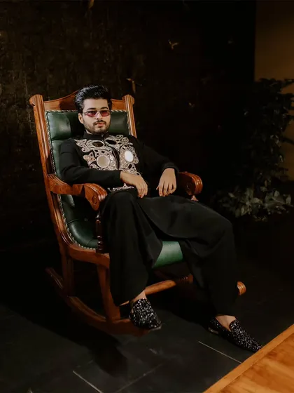 A relaxed portrait of the groom seated in a rocking chair, looking cool and confident in his Sangeet attire.