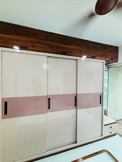 A wide, floor-to-ceiling sliding wardrobe in a two-tone design of beige and dusty rose. The wooden loft cabinets above provide additional storage for less frequently used items.