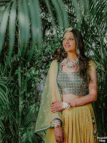 A beautiful portrait of the bride, her yellow Haldi outfit contrasting perfectly with the lush green foliage behind her.