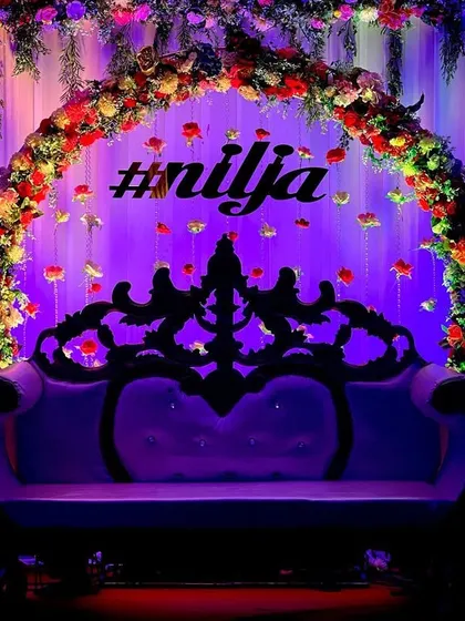 We created this dramatic and elegant seating area for a baby shower. A lush floral arch frames a classic carved sofa, all illuminated by deep purple uplighting to create a rich and luxurious atmosphere for the parents-to-be.