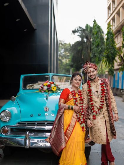 A full-length shot of the couple with the bright blue vintage car, showcasing their traditional attire and the unique prop.