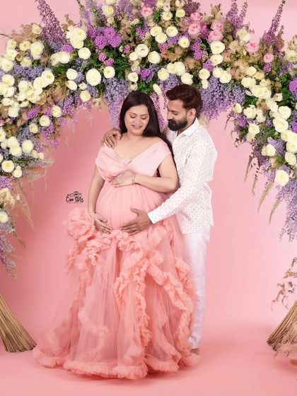 Surrounded by flowers, this couple is ready to welcome their little one. She looks radiant in a pastel pink ruffled gown, creating a soft and romantic vibe for their studio maternity shoot.