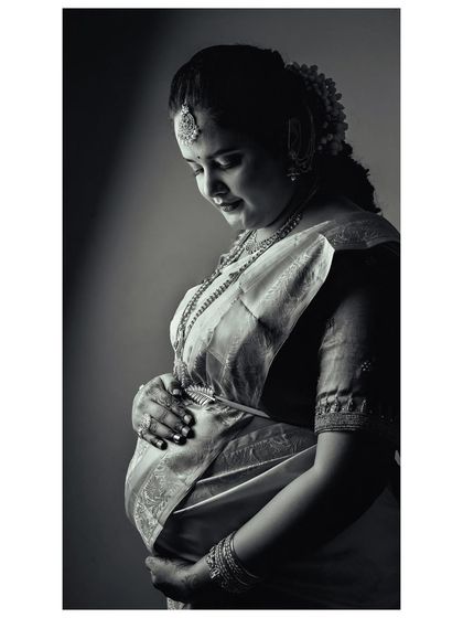 A classic black and white silhouette portrait of a mother-to-be in a traditional saree. The dramatic lighting beautifully highlights her profile and the curve of her belly, creating a timeless and artistic image.
