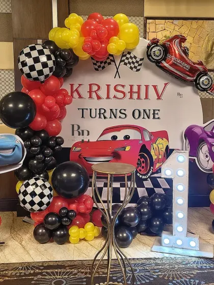 A high-energy Cars theme for Krishiv's first birthday. The setup includes a custom backdrop, character standees of Lightning McQueen, and a balloon arch in the theme's signature red, black, and yellow colors.