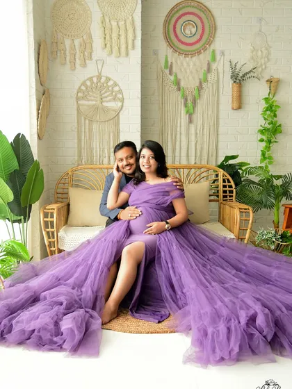 This couple's portrait showcases our popular boho-chic setup, complete with a rattan bench and macrame wall hangings. The vibrant purple gown adds a beautiful pop of color to the bright, natural-light studio setting.