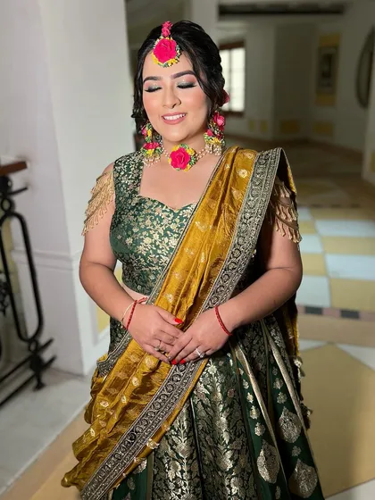 The full look for this Mehendi bride. The green and gold banarasi lehenga is beautifully complemented by the pink floral jewelry and the soft, glamorous makeup.