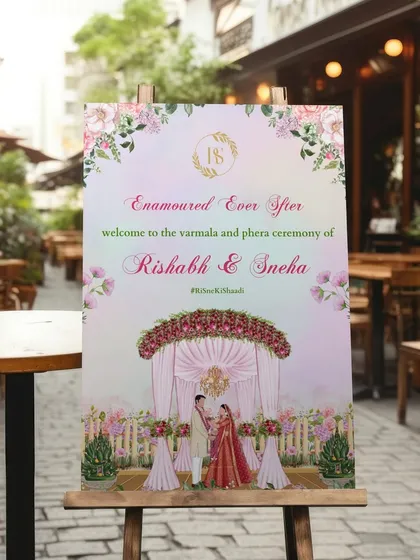 "Enamoured Ever After." This romantic welcome sign for Rishabh and Sneha's Varmala and Phera ceremony features a beautiful illustration of the couple under a floral mandap, set against a soft, dreamy watercolor background.