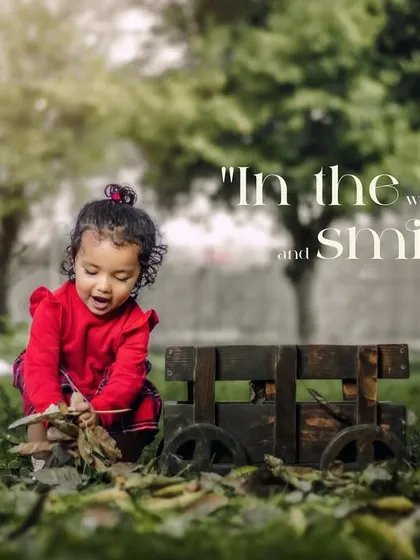 In the world of make-believe and smiles. A girl in red plays with leaves on the ground next to her wooden wagon.