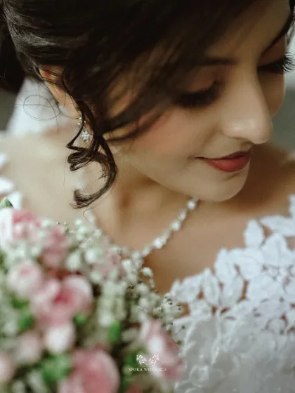 An artistic shot focusing on the bride's gentle expression and the beautiful bouquet she holds, with her necklace and dress details softly blurred.