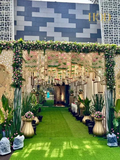 The full view of a spectacular outdoor entrance, featuring a green walkway, golden jali arches, and a ceiling dripping with flowers and lights.