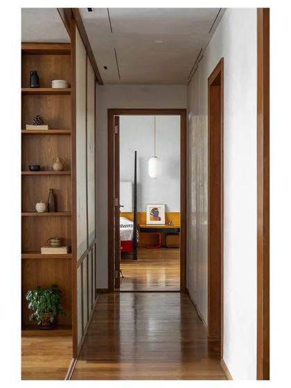A view down a hallway, framed by teak doorways and paneling, looking into one of the bedrooms. This shot emphasizes the home's cohesive material palette and the creation of beautiful vistas within the apartment.