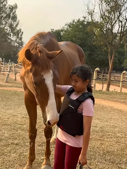 Safety and connection are paramount. A young camper, equipped with a protective vest, shares a quiet moment with her horse, showcasing the gentle and trusting environment we cultivate for both our riders and animals.