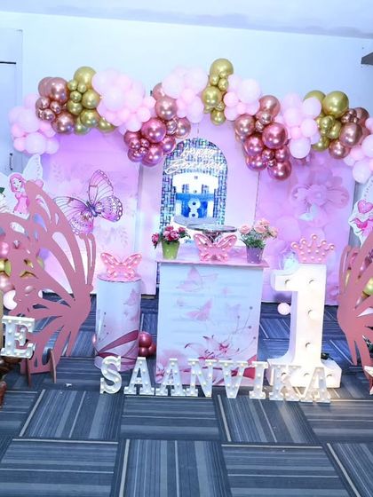 The main stage for a butterfly-themed first birthday, featuring large wing cutouts, a marquee 'ONE', and themed pedestals.