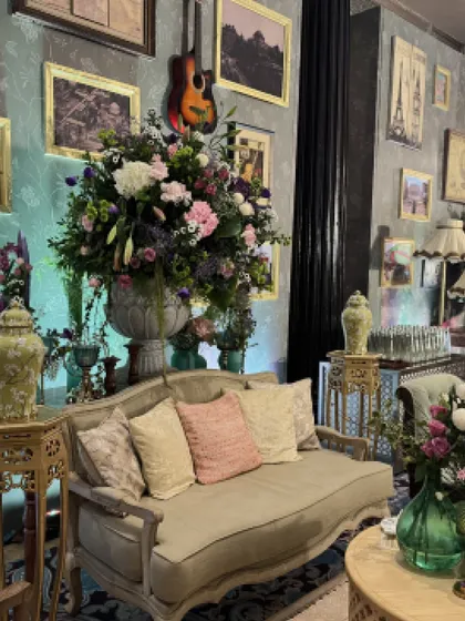 A luxurious lounge area with a gallery wall of framed pictures, oversized floral arrangements, and vintage-style furniture, creating a rich and eclectic look.