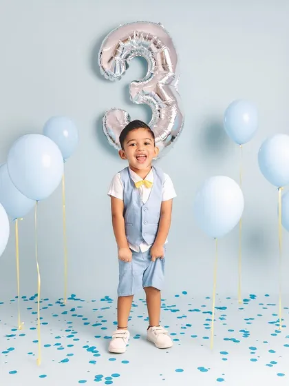 The pure joy of turning three! This little boy is having the time of his life celebrating with blue balloons and confetti.