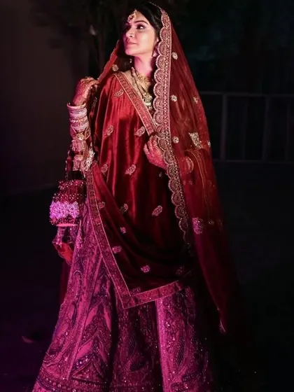 A portrait of the bride in her magnificent red velvet lehenga. The rich color and texture of her outfit, combined with her confident pose, create a truly regal image.