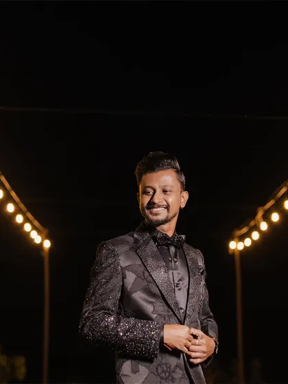 A dapper portrait of the groom in his sparkling tuxedo, smiling under the warm glow of string lights.