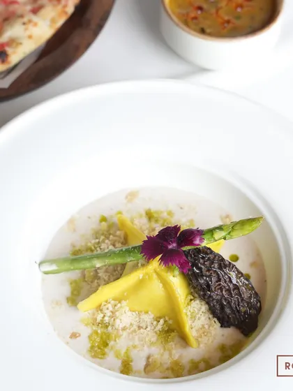 A plated Butternut Squash Manti, showcasing the beautiful stuffed morel, asparagus spear, and edible flower. This dish is a perfect example of our global culinary inspiration.