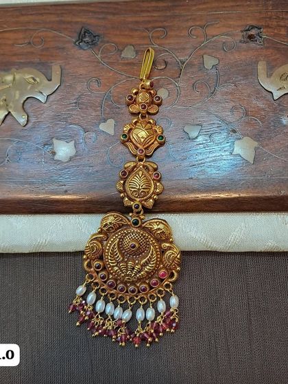 A beautiful temple-style maang tikka with a peacock motif, crafted from 92.5 silver with gold plating. This piece is finished with ruby-colored stones and pearl drops.