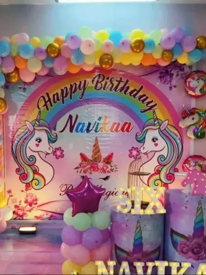 A rainbow unicorn party with a large, colorful backdrop. The setup includes unicorn-themed pedestals and a pastel balloon garland.