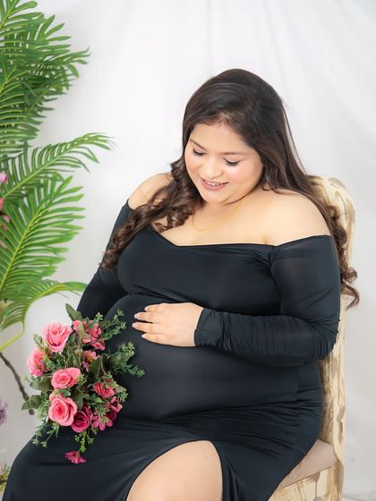 A close-up shot focusing on the connection between mother and baby. She holds a bouquet of pink roses close to her bump, a sweet and tender gesture.