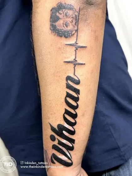 This cover-up tattoo transforms an old piece into a heartfelt tribute to a son. It features his portrait, name, and a heartbeat line, symbolizing that he is forever in his father's heart.