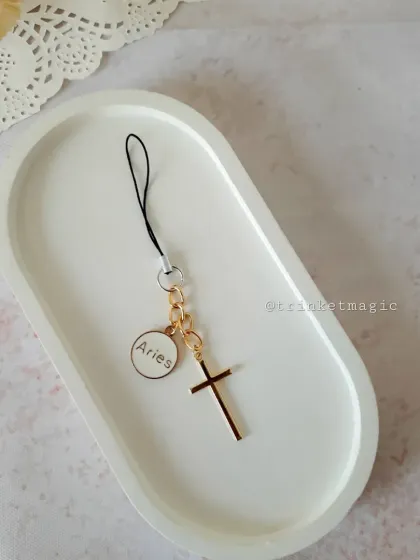 This phone charm is for the faithful and astrological-minded, featuring a cross and an Aries zodiac charm. It's a simple, meaningful accessory.