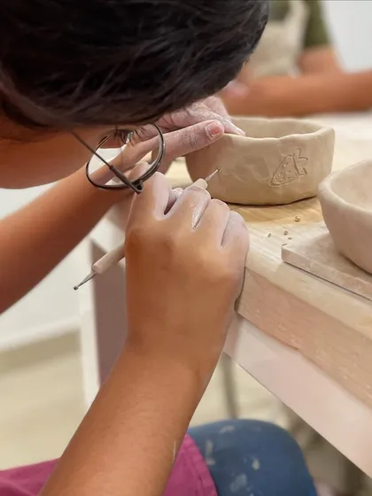 A student uses a needle tool to etch a delicate design onto their hand-built bowl, adding a personal touch.