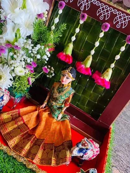 A beautiful gift platter we designed for a half saree ceremony. It features a doll dressed in a traditional orange and green saree, set against a backdrop of woven palm leaves and fresh flowers.