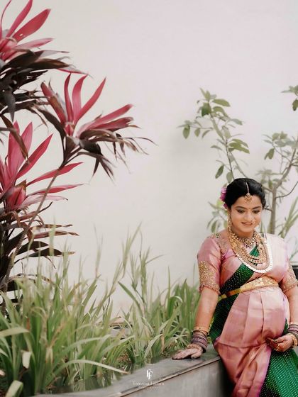 A serene solo portrait of the mother-to-be, seated amidst lush greenery. Her gentle smile and traditional pink saree create a picture of peaceful anticipation.