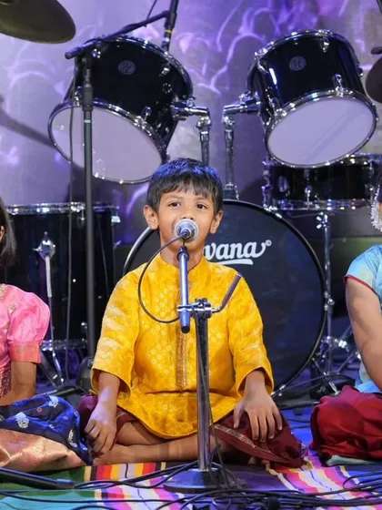 Three of our youngest performers seated on stage, fully focused as they sing devotional bhajans. We encourage students of all ages to connect with traditional Indian music.