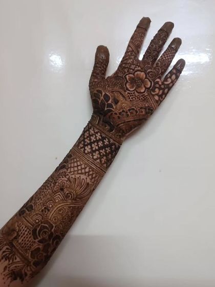 A full view of a single arm, showcasing a complete bridal mehendi design from fingertips to mid-forearm.