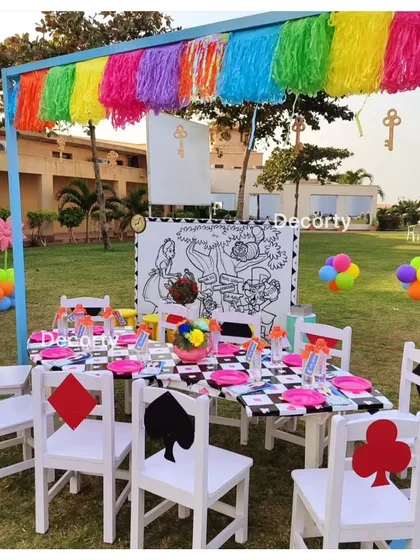 Down the rabbit hole to a whimsical kids' table at an Alice in Wonderland party. The checkered tablecloth, card-themed chair backs, and a giant coloring board create an immersive and fun space for little guests.