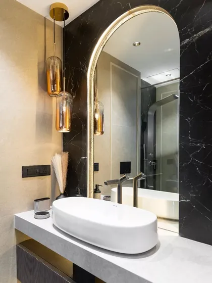 I believe bathrooms should feel like a personal retreat. This design blends a dramatic black marble accent wall with warm gold lighting and an arched mirror to create a sense of modern luxury. The floating vanity and minimalist fixtures complete this harmonious and timeless look.