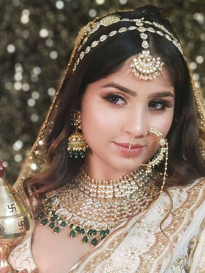 A bride in a white and gold lehenga holding a traditional kalash, adorned with a green-beaded Kundan set. A perfect blend of tradition and elegance.