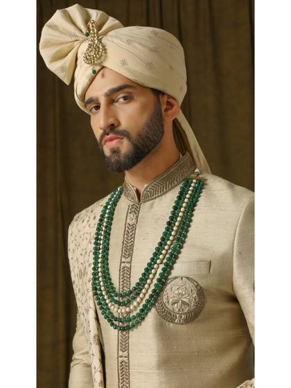 A close-up of the 'VASUDEVA' sherwani, showing the rich texture of the fabric and the intricate detailing on the collar and chest emblem. This piece is designed to command attention.